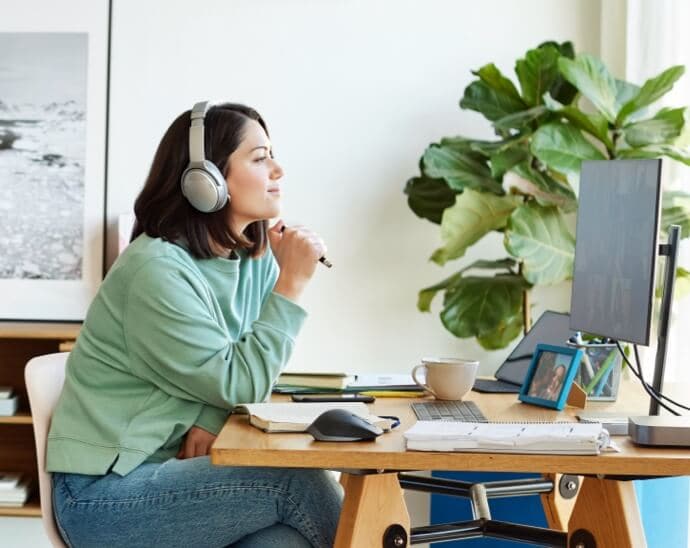 Frau mit Kopfhörern und Stift in der Hand beim Betrachten eines PC-Monitors