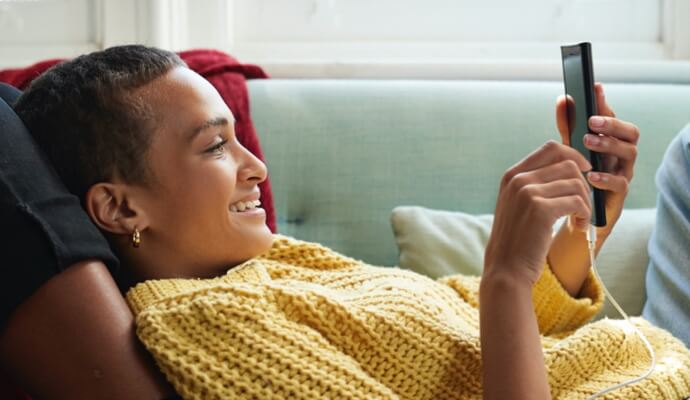 Auf ihr Handy schauende Frau auf dem Sofa beim Starten von Norton 360 mit AntiVirus Plus